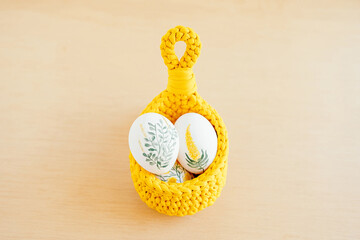 Handmade crochet basket with white chicken eggs painted with flowers placed on wooden table for Easter
