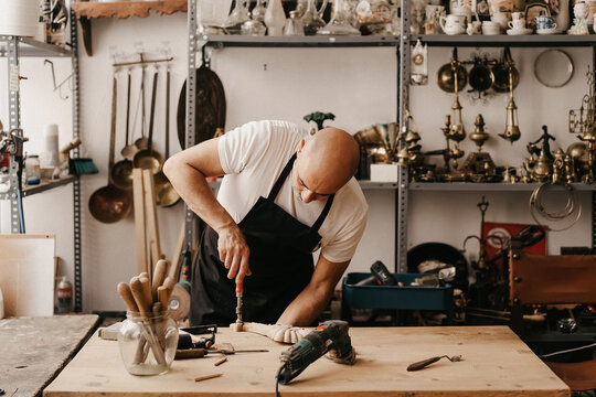 Woodworker In Apron Carving Wood With Chisel And Hammer While Creating Ornate Detail In Workshop