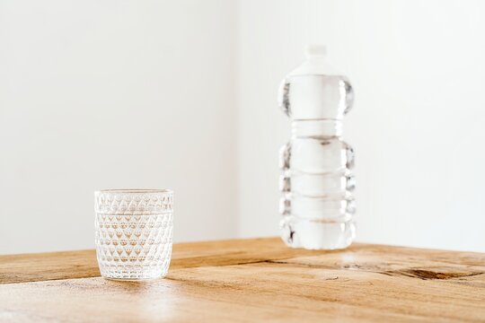 Empty glass and plastic bottle filled with pure fresh water placed on wooden table against white wall
