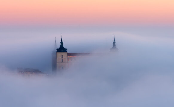 Drone view of peaks of old castles among dense clouds at colorful sunset with hills on horizon in Toledo
