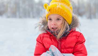 A little girl in a red jacket and a yellow hat laughs in the winter.