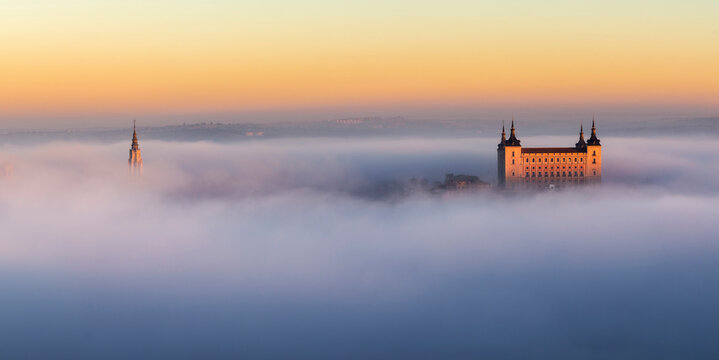 Drone view of peaks of old castles among dense clouds at colorful sunset with hills on horizon in Toledo