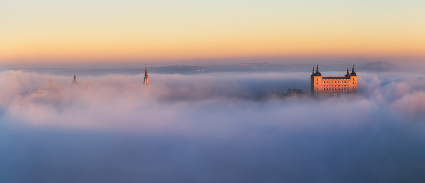 Drone view of peaks of old castles among dense clouds at colorful sunset with hills on horizon in Toledo