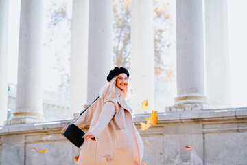 back view of cheerful female tossing fallen leaves while standing in autumn park and having fun at weekend looking over the shoulder