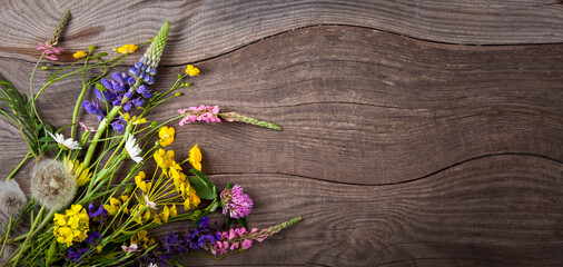 Flowers on old grunge wooden table (chamomile lupine dandelions thyme mint bells rape). Wild nature background