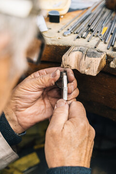 Skilled mature male jeweler in professional goggles creating ring while working at desk with instruments in workshop