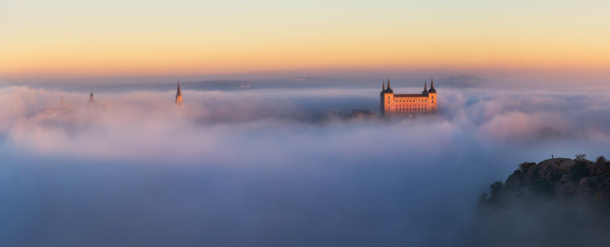 Drone view of peaks of old castles among dense clouds at colorful sunset with hills on horizon in Toledo