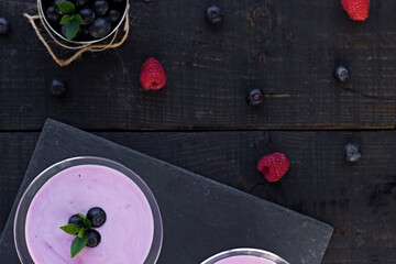 Glass of fresh strawberry and blueberry milkshake, smoothie and fresh strawberries on pink, black and wooden background.