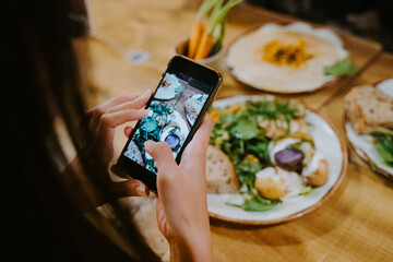 From above cropped unrecognizable female at table taking photo of food on smartphone for social media