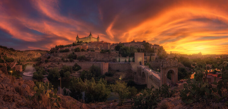 View across river of old city Toledo in Spain with medieval castles and fortresses at sunset time with cloudy sky and reflection in river water