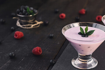 Glass of fresh strawberry and blueberry milkshake, smoothie and fresh strawberries on pink, black and wooden background.