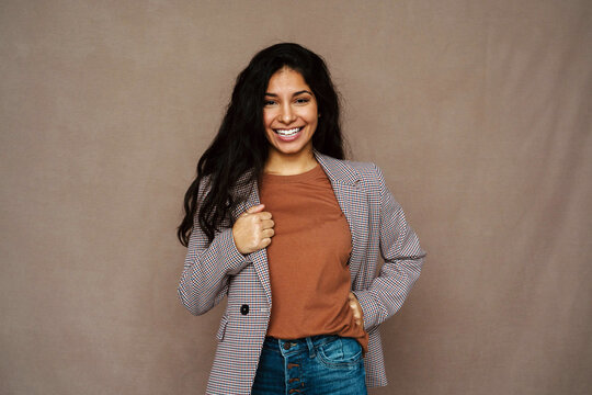 Delighted ethnic female in casual jacket laughing looking at camera on brown background in studio