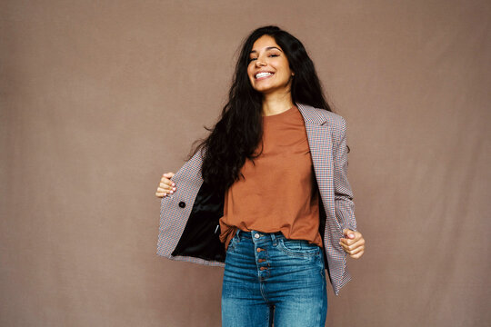 Delighted ethnic female in casual jacket laughing looking at camera on brown background in studio