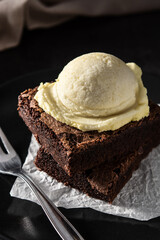 Brownie with vanilla ice cream scoop on black stone. Close up