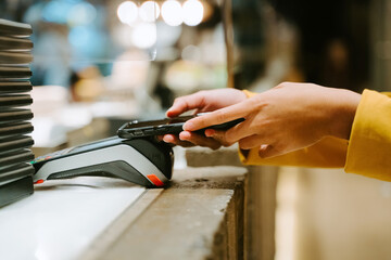 Unrecognizable crop female buyer using smartphone for payment on POS terminal in city