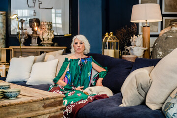 Calm mature female in long elegant dress sitting on couch with dog and enjoying weekend in luxury house while looking at camera