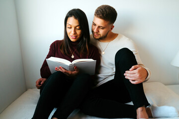 Tender couple sitting on comfortable bed and reading interesting book together