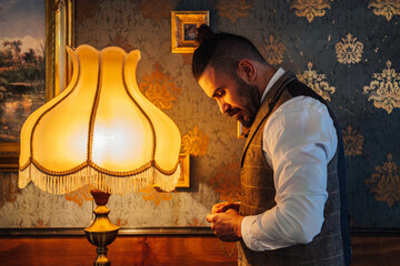 Side view of serious bearded man with chain in hand standing near old fashioned lamp in classic room