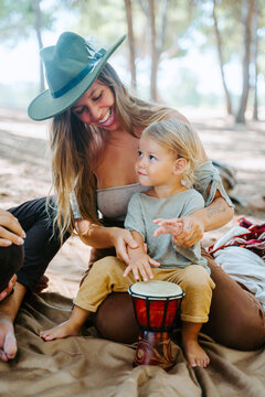Delighted mother and crop father teaching little kid playing bongo drum while spending time together in woods