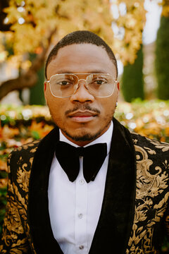 Elegant African American male wearing expensive tuxedo walking along street and looking at camera