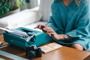 Crop view of anonymous female author sitting on sofa and using vintage typewriter while creating interesting story