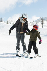 Fototapeta na wymiar Mother and her little son learn to ski toegether at winter time on a snow covered slope.