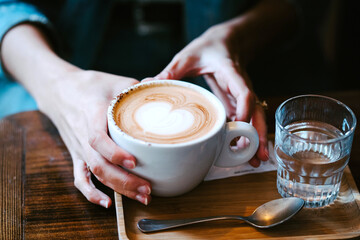 Crop anonymous female holding cup of fresh hot aromatic coffee and glass of water in cafe