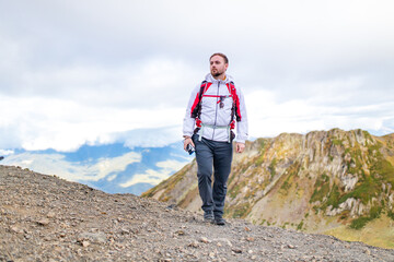 Fototapeta premium Young bearded man wearing white puff jacket standing near a mountain