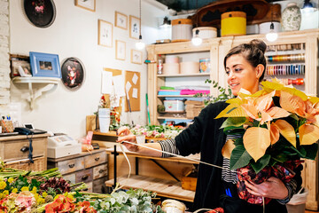 Professional female florist arranging christmas poinsettia flower bouquet while working in shop on wooden table