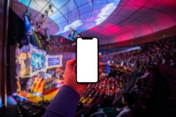 Man's hand using digital application on the mobile smart phone at esport event at big arena. Blank screen with copy space.