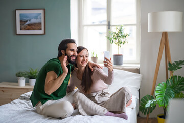 Young couple taking selfie on bed indoors at home.