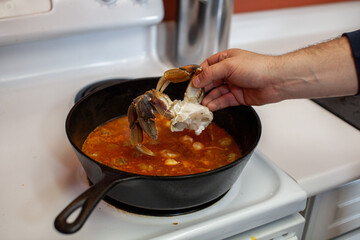 Dungeness crab legs are being put into a large, cast iron pan to make a seafood chowder (soup) for dinner