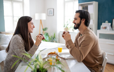 Young couple in love eating hamburgers indoors at home.