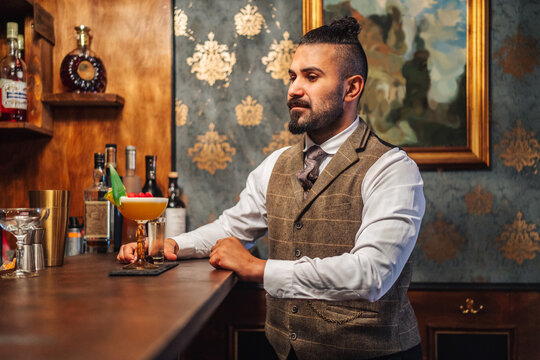 Adult elegant man smelling liquor near tropical cocktail while sitting at counter and resting in bar