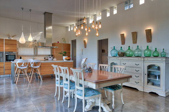 Interior of modern kitchen in apartment with wooden dining table and glowing lamps hanging from ceiling