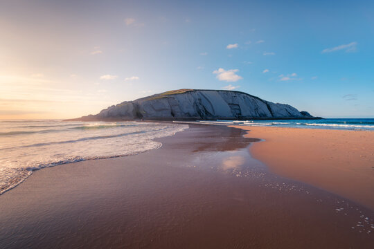 Picturesque scenery of chalk cliff located on amazing Playa de Covachos sandy beach washing by foamy sea from both sides against sunset sky in Cantabria