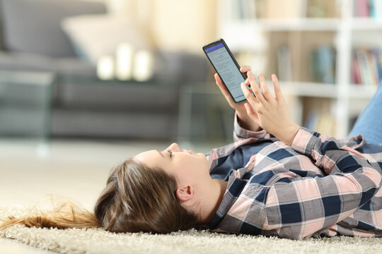Teenager using smart phone lying on the floor at home
