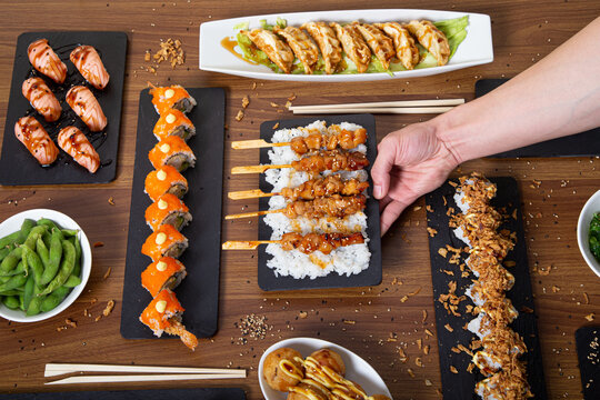 Top view of unrecognizable person with assorted sushi and rolls arranged on wooden table in restaurant with Asian food