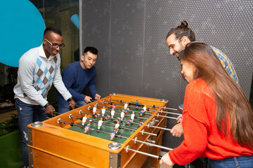 Cheerful young multiethnic people in casual clothes having fun and playing table football together