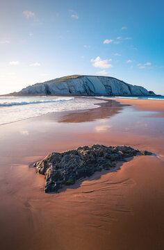 Picturesque scenery of chalk cliff located on amazing Playa de Covachos sandy beach washing by foamy sea from both sides against sunset sky in Cantabria