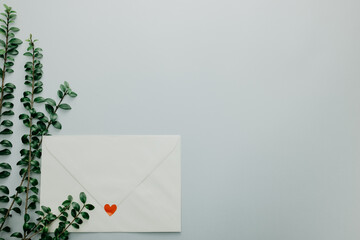 Minimal composition with a white envelope, heart and green leaves