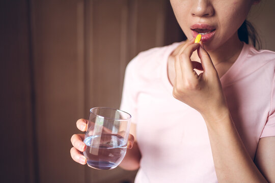 Crop unrecognizable female with glass of fresh water taking yellow vitamin pill while representing healthy lifestyle concept