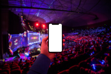 Man's hand using digital application on the mobile smart phone at esport event at big arena. Blank screen with copy space.