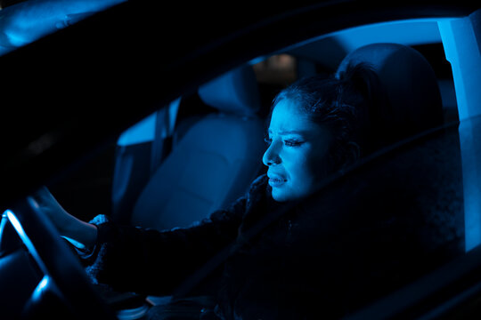 Side view of unhappy young female thinking about problems and crying while driving automobile at night