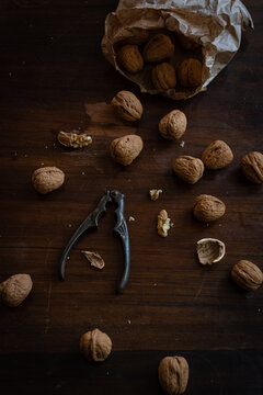 From above of pile of whole and cracked walnuts with kernels placed with nutcracker on dark wooden surface