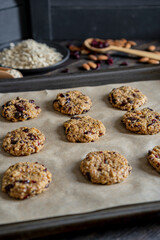 Oatmeal cranberry round cookies before oven, homemade healthy vegan snack or biscuits. Homemade nut bars on baking sheet with ingredients for cooking  on rustic table. Selective focus, copy space