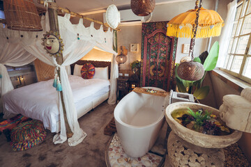 Cozy bed with canopy and white bathtub located in hotel room with traditional oriental furniture and decorations in Taiwan