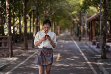Ethnic Asian female using smartphone and walking along Tanya Shen Green Bikeway in Taichung