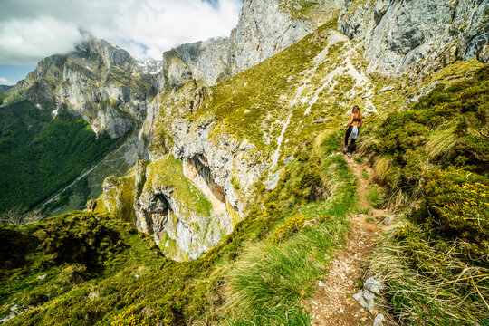 Unrecognizable female hiker in activewear exploring nature in spectacular rocky mountainous valley covered with green grass in Fuente De