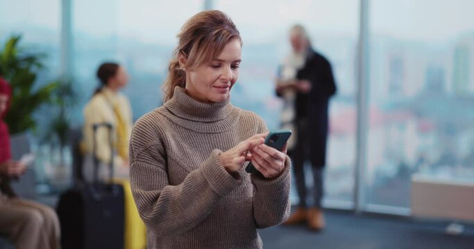 Attractive Millennial Woman Browsing Apps on Smartphone Screen Texting Messages in the Longe Area. Airport Terminal. Passengers. Travel Concept.